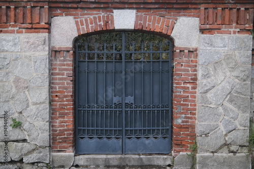 Fotografie Closed iron gate with decorative metal bars set within an old brick arch and stone wall, showing traditional masonry and historic architectural detail