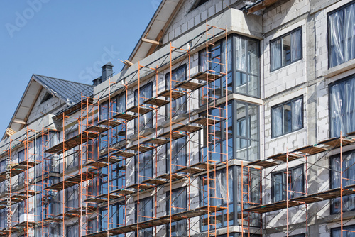 Residential building facade under construction with metal scaffolding and windows. Urban renovation and construction process concept showing apartment building development and exterior work.