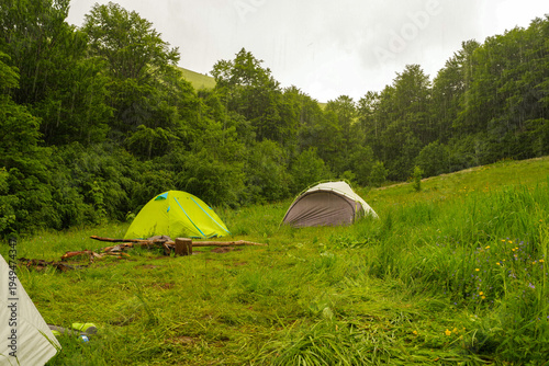Two colorful camping tents on a forest glade during rain.