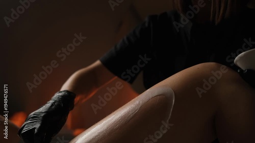 Professional beautician in black gloves applying cream on a client's leg with a spatula