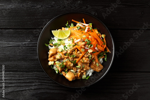 Chicken Satay with rice, roasted peanuts and greens in a black bowl
