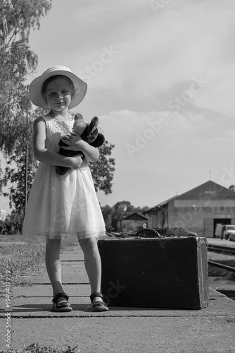 Young girl with teddy bear and vintage suitcase on train station platform
