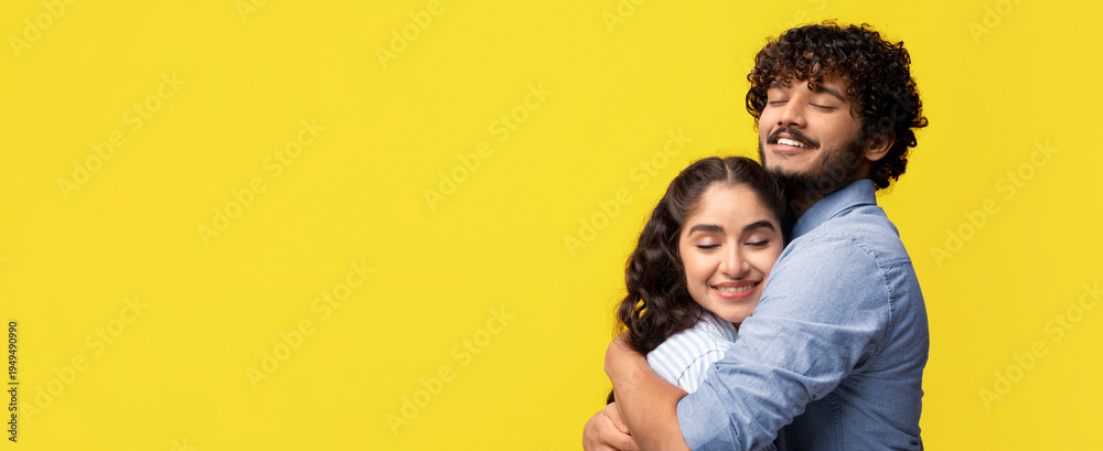 Fototapeta premium A couple stands together in a studio with a bright yellow background. They are embracing each other with smiles on their faces. The scene shows love and connection between them.