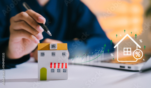 Fotografija Mortgage rate concept, hand with pen near house model and rising percentage grap