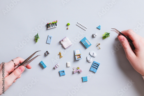 Miniature toy house parts and children's hands with tweezers on a blue background