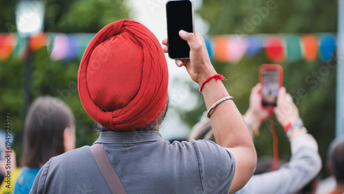 Photography Sikh man in red turban filming celebration with smartphone at India Day in Mosco