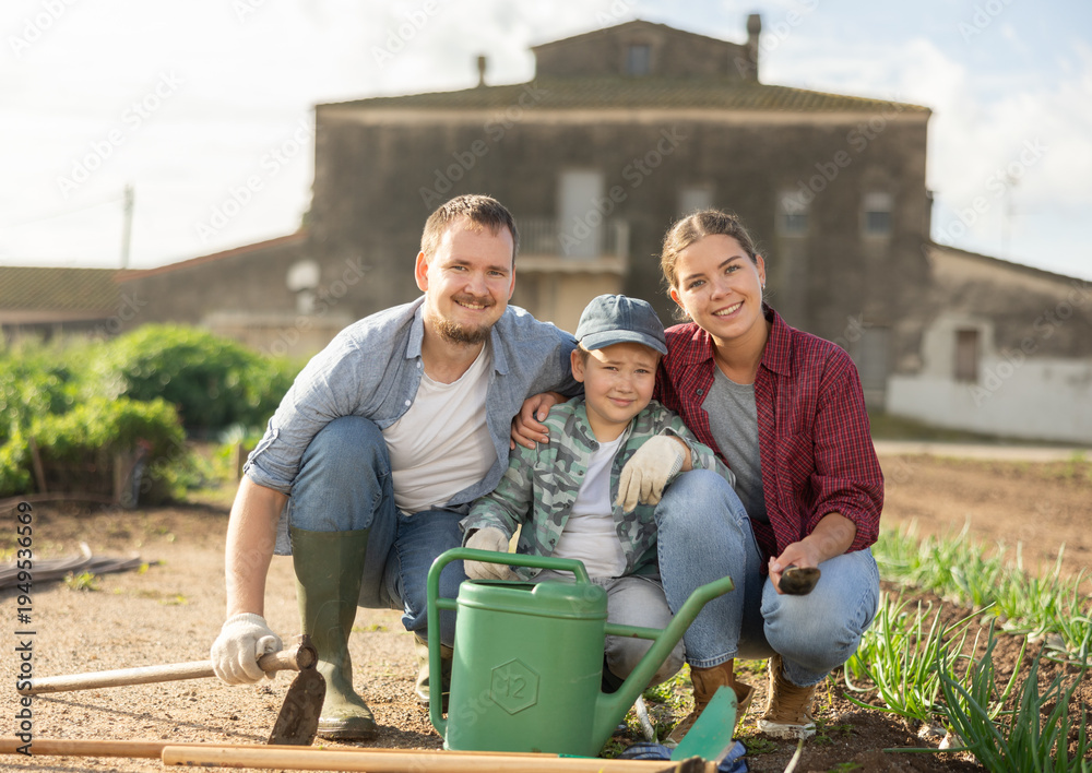 Fototapeta premium Family of farmers with a watering can and a hoe in the garden after planting seeds. Farmers grow organic and organic vegetables. Portrait of a family on a farm