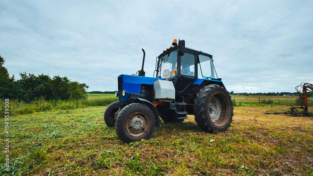Obraz premium Blue tractor parking in harvested field after mowing grass
