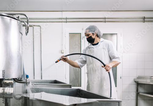 Worker cleaning dairy factory equipment with water hose