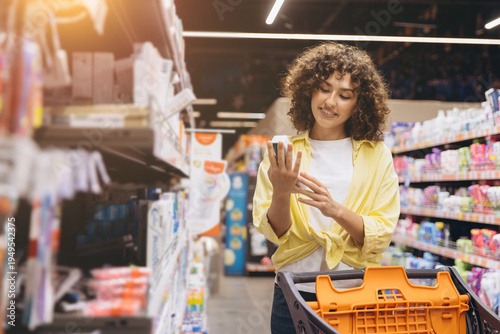 Canvas Print Smiling woman shopping at grocery store, comparing product labels and making pur