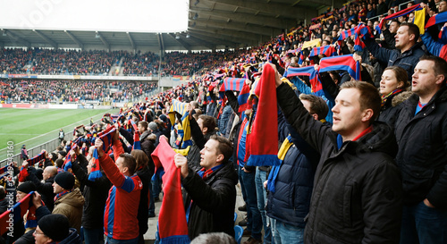 Passionate football supporters cheering in a crowded stadium stands while holding up team scarves during an intense match as a symbol of sports fandom loyalty and the exciting atmosphere of a live gam