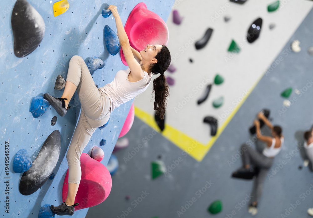 Fototapeta premium Motivated young girl climbing without ropes and harnesses on artificial bouldering wall in modern fitness center