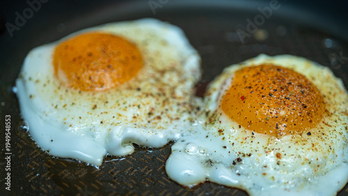 Valokuva Close-up macro of two fried eggs with black pepper and spices in a frying pan