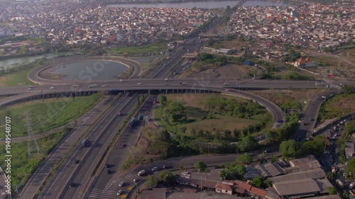 High-angle drone shot of the Dupak toll road in East Java, featuring flowing traffic on multi-lane expressways and intricate cloverleaf-style connections during a clear afternoon