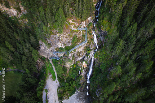 Aerial view of Verpeilschlucht waterfall and hanging walkway in Kaunertal, Austrian Alps. Stunning mountain gorge with forest, hiking trail and cascading stream in Tyrol, Austria.