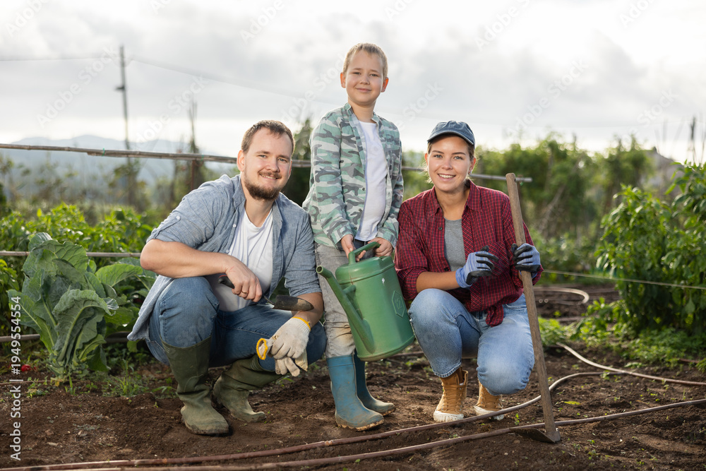 Fototapeta premium Family of farmers with a son in the garden after planting seeds. Generation of farmers grows quality products. Farmers plant seeds in cultivated land