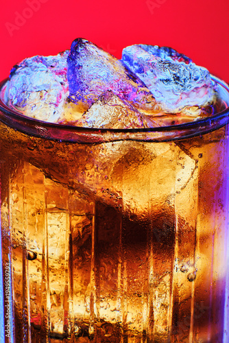 Macro photo of a glass with a carbonated drink and ice cubes. Contrasting blue and purple neon lights on the ice on a rich red background. Concept of nightlife, party