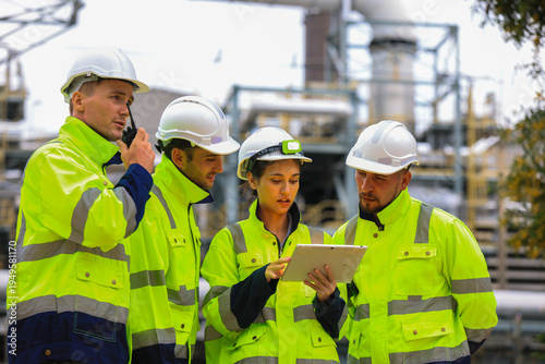 Industrial Engineer Using Digital Tablet for Predictive Maintenance in Oil and Gas Refinery. Team of Engineers Discussing Safety Protocols at Large Scale Oil Refinery Facility.