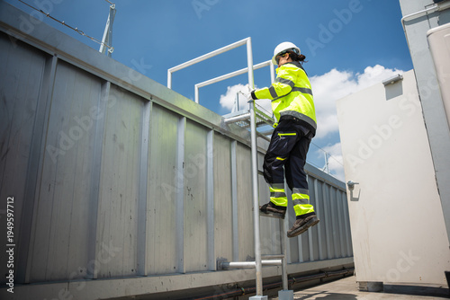 Professional maintenance worker in hard hat and safety gear ascending to inspect HVAC systems, Woman engineer climbing a metal ladder for technical installation at construction site