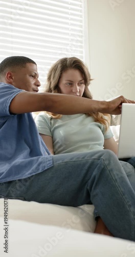 Vertical video: Diverse couple typing on laptop following pointing on couch discussing goals