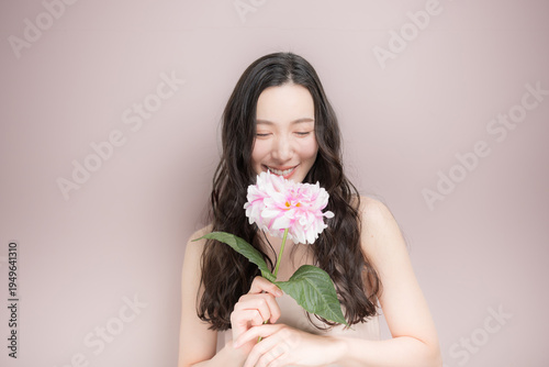 ダリアの花を持って多幸感にあふれるピンクの春色イメージの女性の美容ビューティーイメージ　ピンク背景の上半身