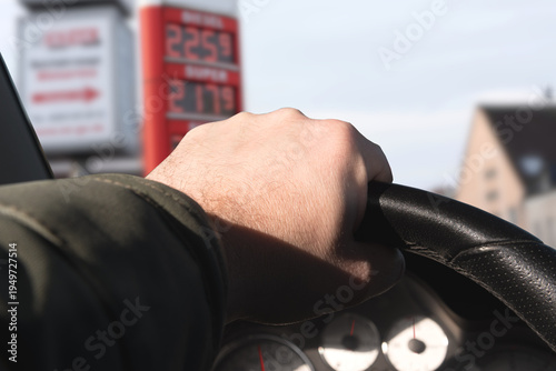 Ein Mann fährt einen Wagen zu einer Tankstelle. Preistafel zeigt hohe Kraftstoffpreise.