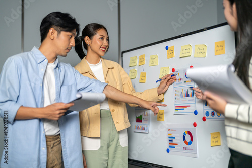 Asian happy business team discussing data charts and project plan on whiteboard in office, Young startup colleagues brainstorming marketing strategy, Corporate teamwork and presentation concept