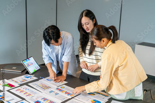 Asian digital marketing agency team analyzing SEO and ads performance on table, Young business professionals discussing campaign metrics, conversion rate and online marketing strategy concept
