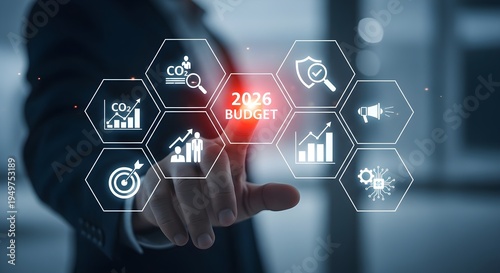 Close-up of a businessman's hand interacting with a virtual 2026 budget interface with various financial icons in a dark office.
