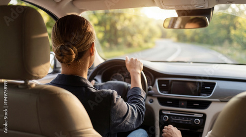 Tableau sur toile Rear view of an elegant woman driving a modern car on a scenic, winding country road during a beautiful golden hour