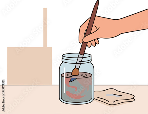 A hand paints an illustration of a fish in a jar with a brush on a table.