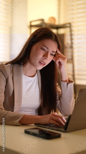 Asian businesswoman working late on laptop, touching head in frustration, adult female professional under pressure from workload, stress, problem solving, corporate challenge determination in business