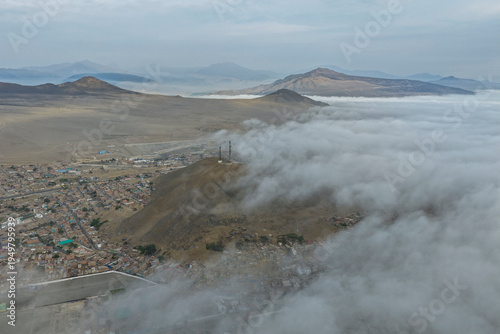 Aerial view of desert mountains and city with many low clouds