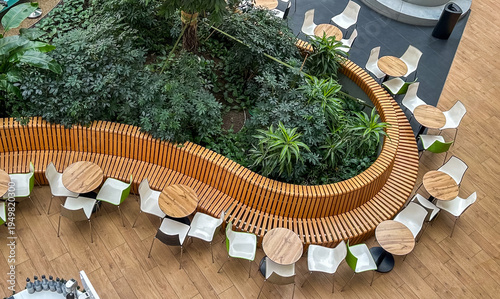 High angle view of modern indoor cafe with circular wooden bench and lush green plants
