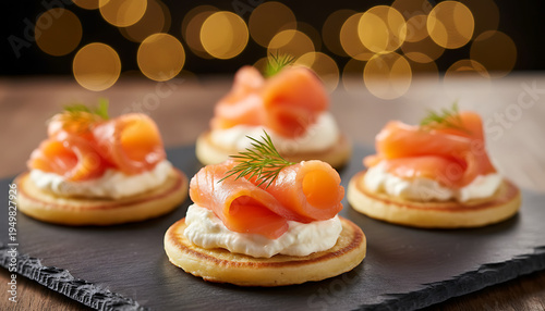 Smoked salmon appetizers arranged on slate. Small cornbread cakes topped with cream cheese, salmon, and dill. Cozy bokeh lights add festive atmosphere for parties or events. Gourmet Party Appetizers
