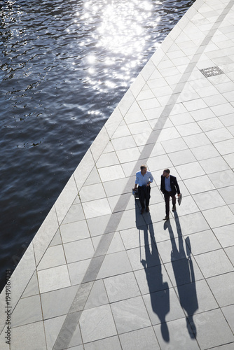 Two businessmen walking and talking at the riverbank
