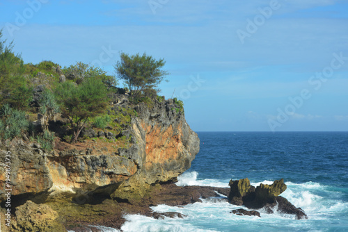 Stunning tropical coastline featuring rugged limestone cliffs and turquoise ocean waves crashing against rocks under a clear blue sky