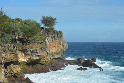 Rugged Limestone Sea Cliffs and Tropical Greenery Overlooking the Deep Blue Indian Ocean with Crashing White Waves at Nguluran Beach, South Coast of Yogyakarta