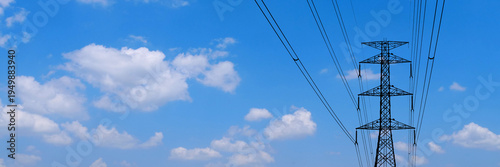 Electric pylon reaching towards the bright blue sky. The image captures the structure against a backdrop of clouds, a testament to modern engineering 