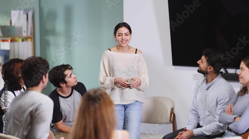Group of interested students listening to young woman speaking in standing position in bright room