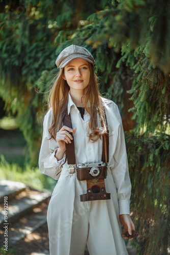 Fotografie portrait of a young woman dressed in classic Gavroche style  — complete with newsboy cap, vest, suspenders, and a vintage film camera in hand