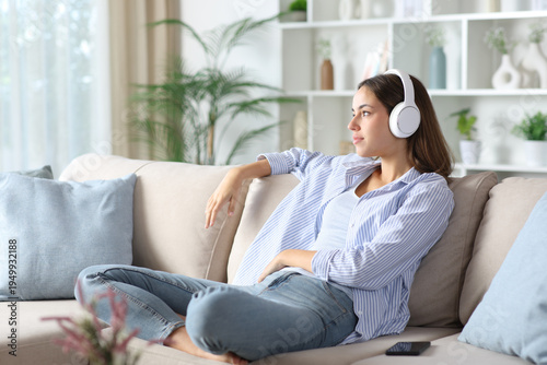 Woman wearing headphone listening audio and looking away at home