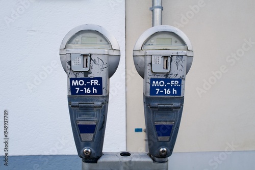 Pair of vintage parking meters — weekday hours sign, urban street detail