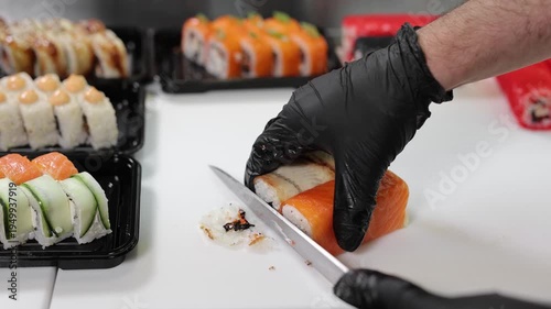 Chef slicing fresh sushi rolls in professional kitchen.