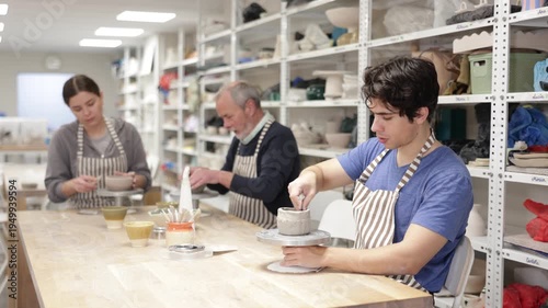 Young woman, young man and elderly man in ceramic workshop sculpting clay products during master class