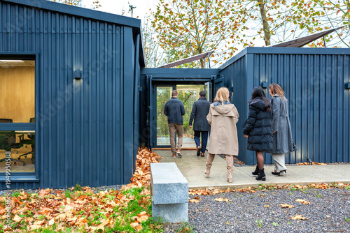 Unrecognizable business team entering in modular office made from repurposed shipping containers with solar panels in a corporate visit or meeting to sustainable workplace, surrounded by autumn leaves
