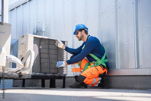 Professional HVAC technician checking air conditioning condenser unit on rooftop during maintenance, Technician performing quality check on industrial air conditioning unit on rooftop exterior
