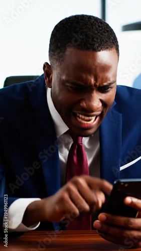 Angry African American businessman looking at smartphone with frustrated expression in office