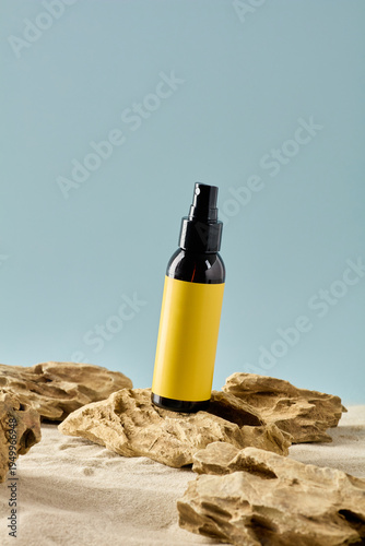 Amber glass spray bottle mockup tilted on rock, yellow label cosmetic packaging in sand, natural sunscreen or essential oil presentation.