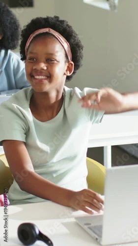 Vertical video: Smiling mint-top girl shifting, raising right hand to answer in class with laptop
